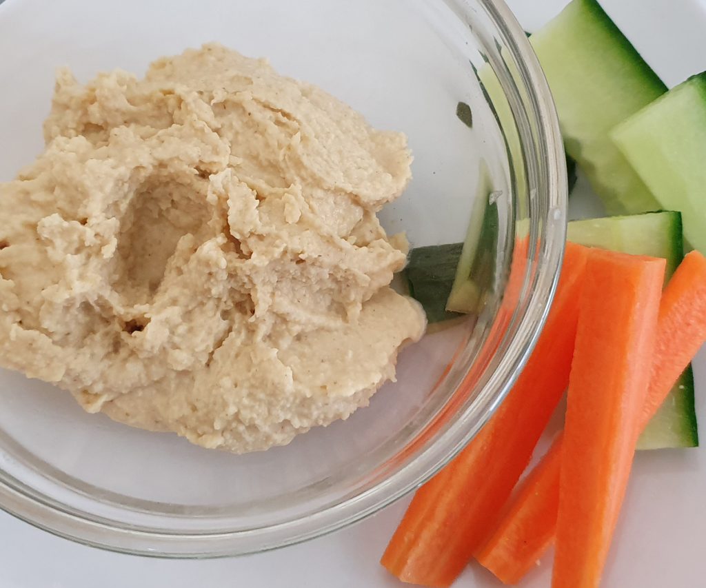 A bowl of hummus with a side of cucumber and carrots